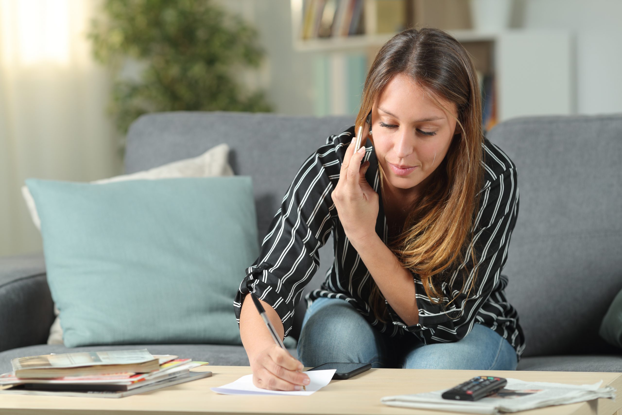 Young women on mobile phone while writing down notes on paper
