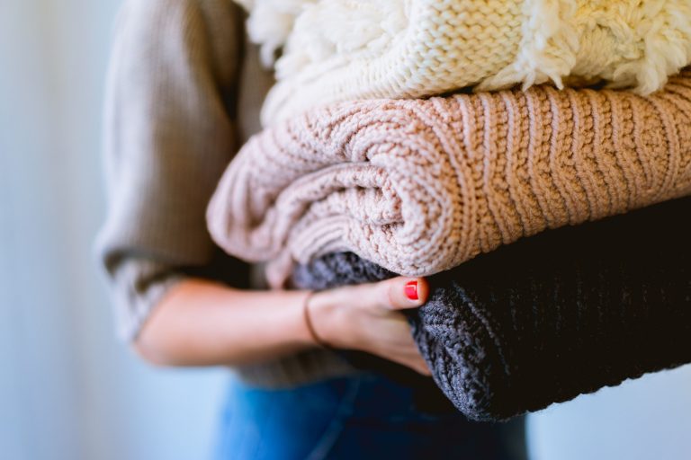 Girl holding stack of 3 knitted jumpers