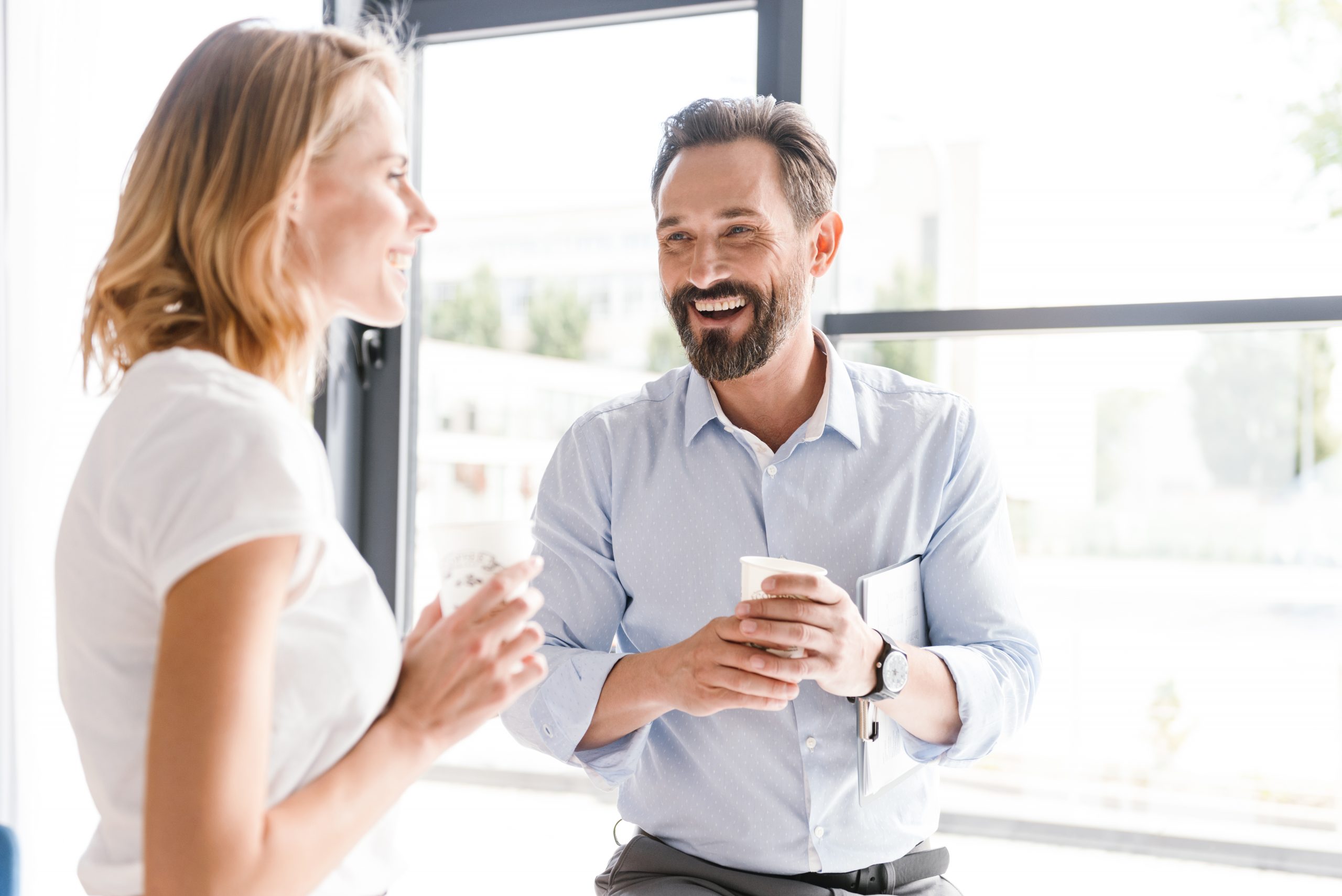 Couple,Of,Cheerful,Colleagues,Talking,While,Standing,At,The,Office