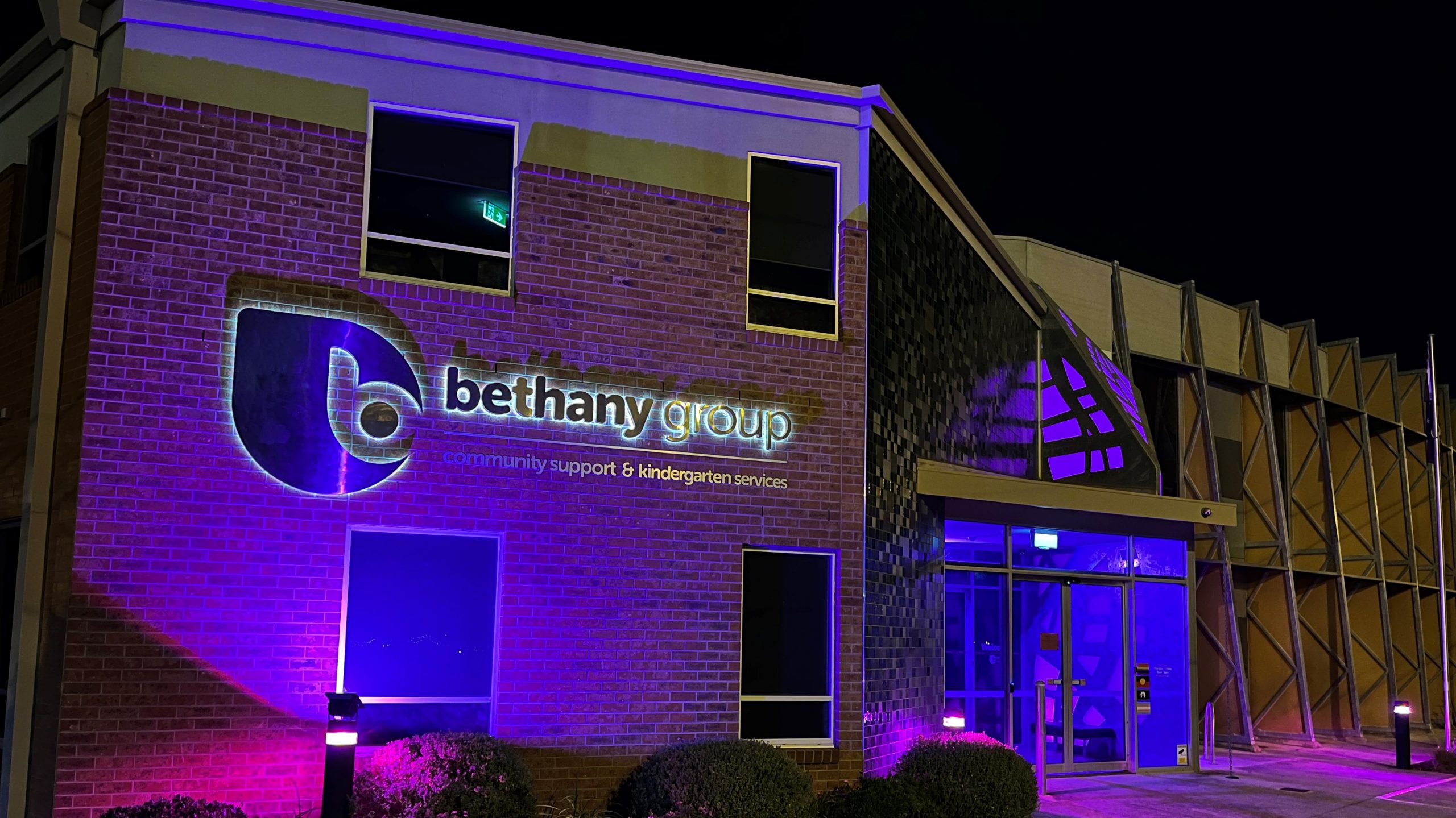 Photo of a two storey office building, lit up with purple lights, with the signage Bethany 